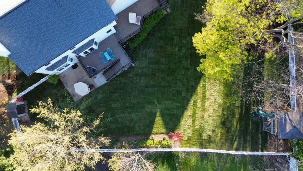 Aerial view of a landscaped backyard with a deck, lawn, trees, and outdoor furniture.
